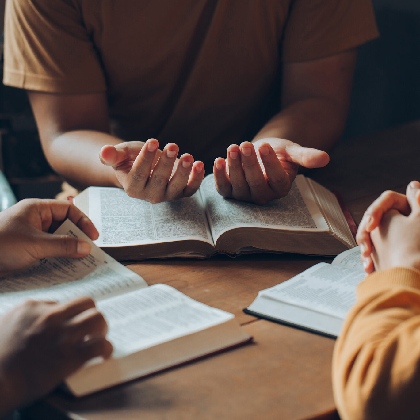 Christians and Bible study concept.Christian family sitting around a wooden table with open bible page and holding each other's hand praying together.